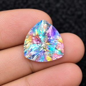 May include: A triangular-cut gemstone featuring a vibrant iridescent finish that displays a spectrum of colors including blue, pink, yellow, and purple. The stone has a faceted surface that reflects light in a starburst pattern.