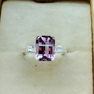 May include: A silver ring with a large, rectangular, purple gemstone and two smaller, clear gemstones on either side.