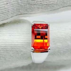 May include: A silver ring featuring a large, rectangular, red and orange gemstone.