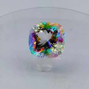 May include: A clear, faceted gemstone with a rainbow of colors, including red, orange, yellow, green, blue, and purple. The gemstone is cut in a cushion shape.