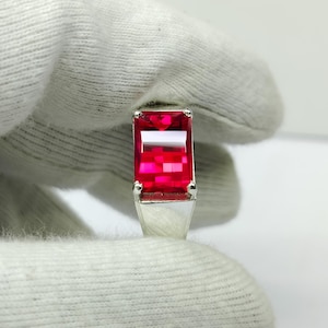 May include: A silver ring featuring a large, rectangular, faceted, bright red gemstone. The gemstone is the focal point, with a clear, vibrant color. The ring's band is a simple, polished silver.