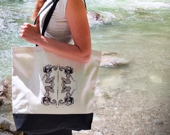 May include: A white canvas tote bag with black handles and a black bottom. The bag has a black and white graphic print of two women in a symmetrical design.