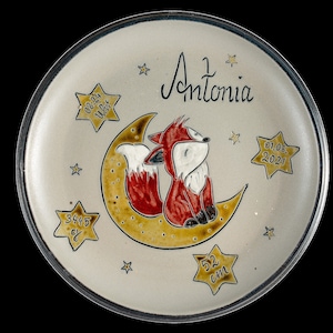 Könnte beinhalten: Ein weißer Keramikteller mit handgemaltem Design eines Fuchses, der auf einem Halbmond sitzt. Der Teller ist mit goldenen Sternen und dem Text "Antonia 1 01.06.2021 3445 g 52 cm" verziert.
