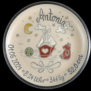 Könnte beinhalten: Handbemalte Keramikplatte mit Babymotiv. Mit dem Namen "Antonia", einem Kinderwagen, Teddybär, Mond, Sternen und Geburtsdetails: Datum, Uhrzeit, Gewicht und 52,0 cm Länge. Die Platte hat einen cremefarbenen Hintergrund mit dunkelblauem Rand.