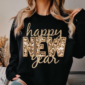 Könnte beinhalten: Schwarzes Sweatshirt mit goldfarbenem Glitzerschriftzug "happy NEW year". Die Buchstaben "NEW" sind mit goldenen Pailletten gefüllt. Ein festliches Kleidungsstück zur Feier des neuen Jahres.