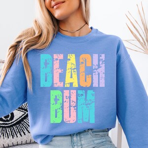 May include: A light blue sweatshirt with the text "Beach Bum" in rainbow colors. The text has a distressed, vintage look.