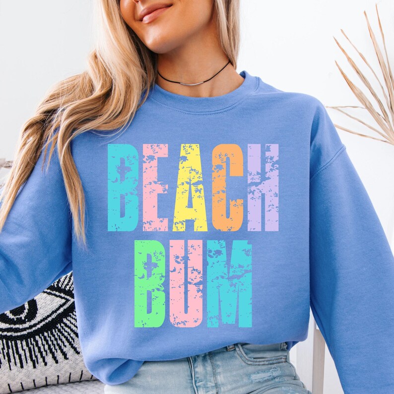 May include: A light blue sweatshirt with the text "Beach Bum" in rainbow colors. The text has a distressed, vintage look.