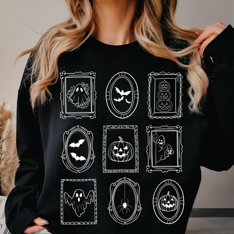 May include: Black sweatshirt featuring a repeating pattern of framed Halloween-themed illustrations. The white illustrations include ghosts, bats, pumpkins, and a spider. The frames are in various shapes, including rectangular and oval.