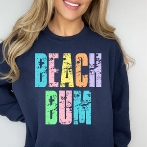 May include: A navy blue sweatshirt with the text "Beach Bum" in rainbow colors. The text is in a distressed font.