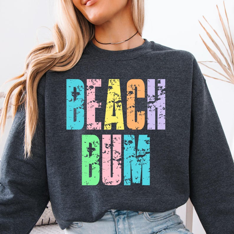 May include: A dark gray sweatshirt with the text "BEACH BUM" in rainbow colors. The letters are distressed and have a vintage look.