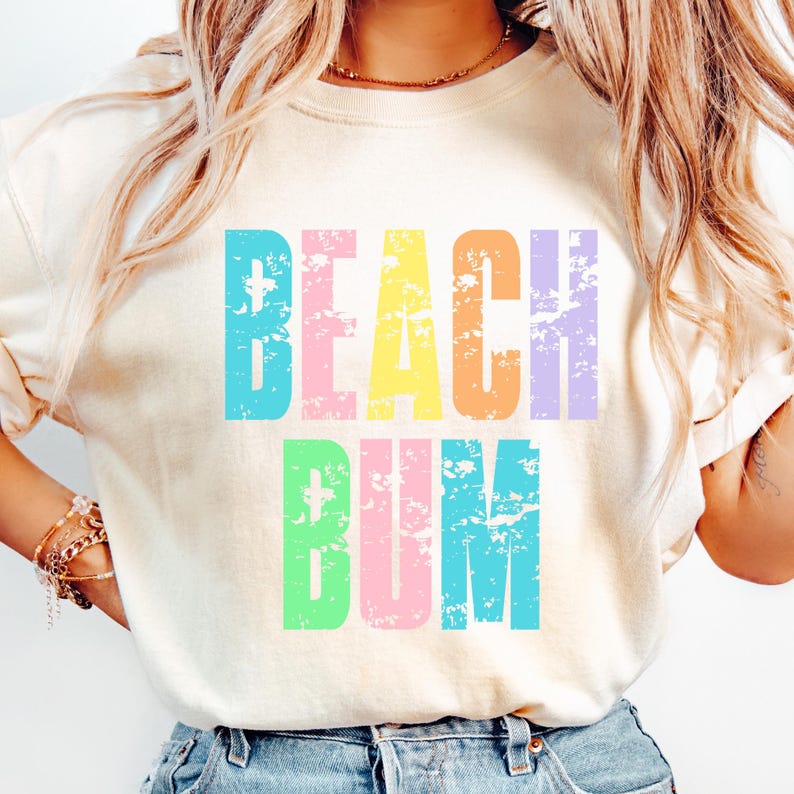 May include: A white t-shirt with the text "Beach Bum" in rainbow colors. The letters are distressed and have a vintage look.
