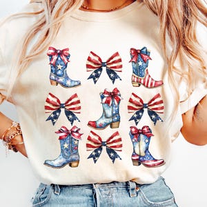 May include: Cream-colored t-shirt featuring a pattern of watercolor cowboy boots and bows in red, white, and blue. The boots have stars and stripes, and the bows have a patriotic design. The overall theme is Americana and Independence Day.