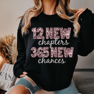 May include: Black sweatshirt with pink glitter lettering that reads "12 New Chapters 365 New Chances".