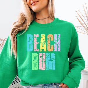 May include: Green sweatshirt with the text "Beach Bum" in rainbow colors with a distressed look.