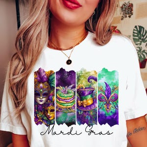 May include: White t-shirt with a colorful Mardi Gras design featuring a mask, a king cake, a hat, and a fleur-de-lis. The text "Mardi Gras" is written below the design.
