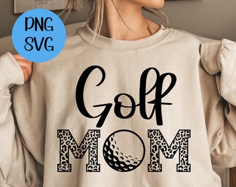 May include: A beige sweatshirt with the text "Golf Mom" in black lettering. The "M" and "O" are decorated with a leopard print pattern. A black and white golf ball is centered between the words.