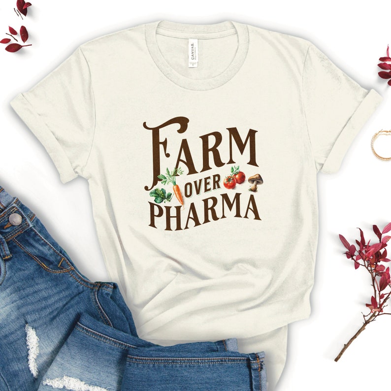May include: A white t-shirt with brown text that reads "Farm Over Pharma" with a graphic of vegetables and a mushroom.