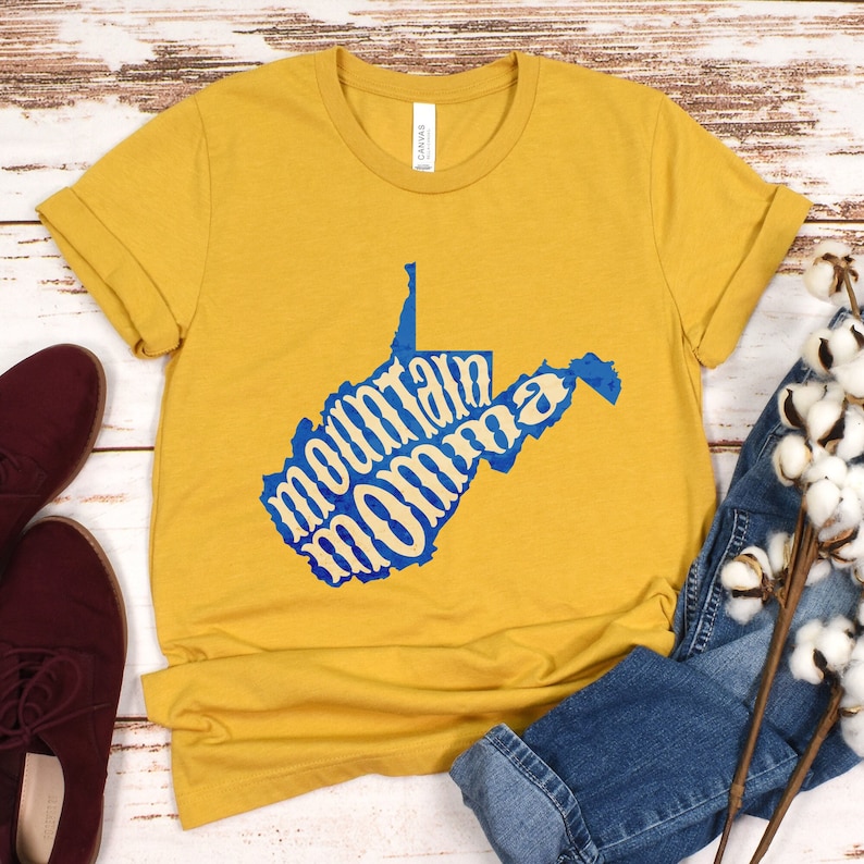May include: A mustard yellow t-shirt with a blue outline of the state of West Virginia. The words "mountain momma" are written inside the state outline.