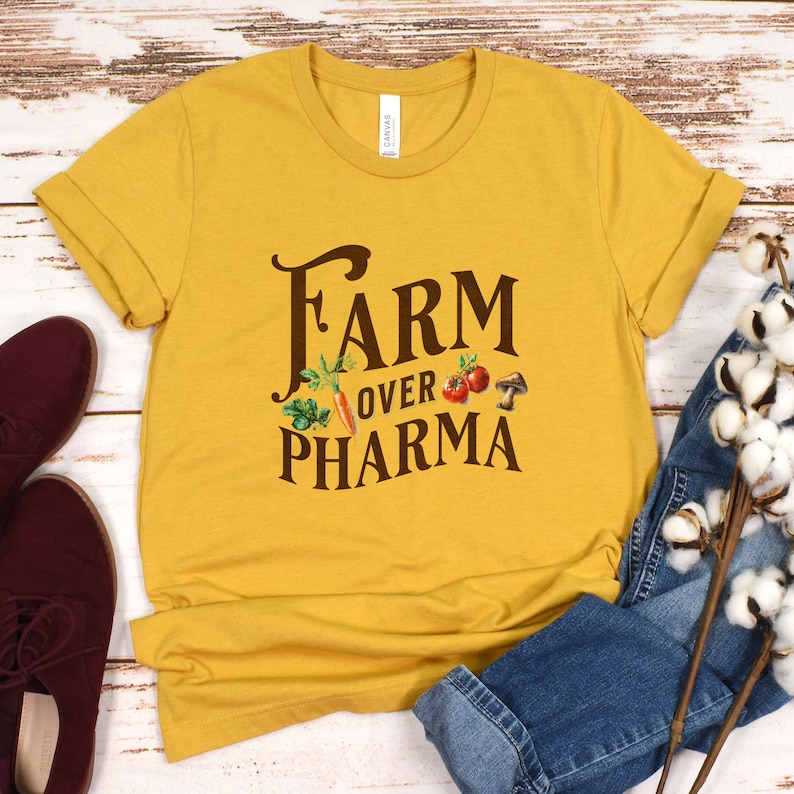 May include: A mustard yellow t-shirt with the text "FARM OVER PHARMA" in brown lettering. The text is surrounded by small images of vegetables and a mushroom.