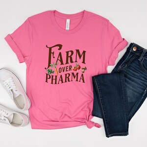 May include: Pink t-shirt with the text "FARM over PHARMA" in brown lettering. The text is surrounded by images of vegetables and mushrooms.