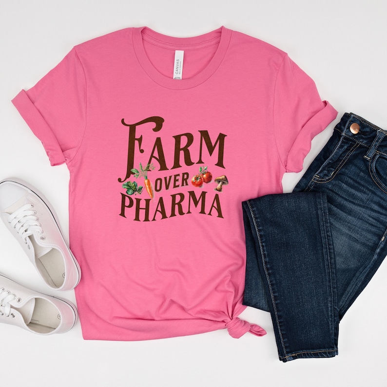 May include: Pink t-shirt with the text "FARM over PHARMA" in brown lettering. The text is surrounded by images of vegetables and mushrooms.