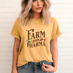 May include: A yellow short-sleeved t-shirt with the text "FARM over PHARMA" in brown lettering. The text is surrounded by a graphic of vegetables and a mushroom.