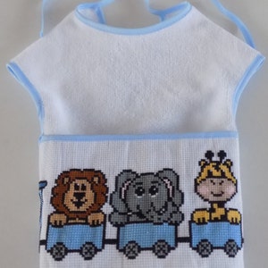 Puede incluir: Babero blanco para bebé con ribete azul y un diseño de punto de cruz de un león, un elefante y una jirafa montando un tren.