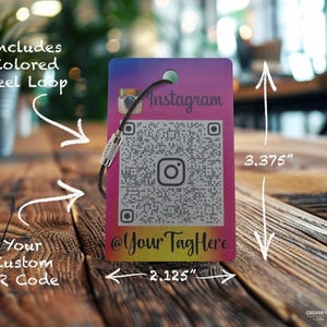 May include: A rectangular Instagram tag with a QR code, measuring 2.125 inches wide and 3.375 inches tall. It features a colored steel loop and the text "@YourTagHere". The tag has a gradient background of pink, purple, and yellow.