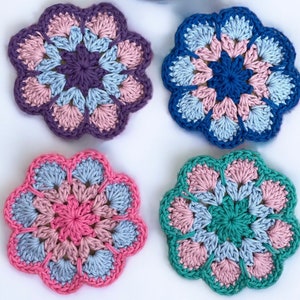 Può includere: Quattro sottobicchieri all'uncinetto a forma di fiore in diversi colori: rosa e viola, blu e bianco, rosa e verde e rosa e blu.