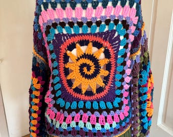 May include: A colourful crocheted sweater with a large, circular, multi-coloured design in the centre. The sweater has long sleeves and a loose fit.