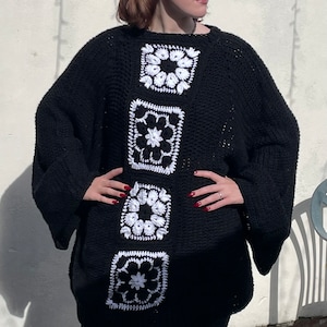 May include: A black oversized sweater with white crocheted flower designs down the front.
