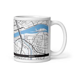 Peut inclure: Mug en céramique blanche avec une carte détaillée de Bâle, en Suisse. La carte présente un fleuve bleu clair et des rues noires. Le mot "BASEL" est imprimé en blanc sur une bande noire au bas du mug.