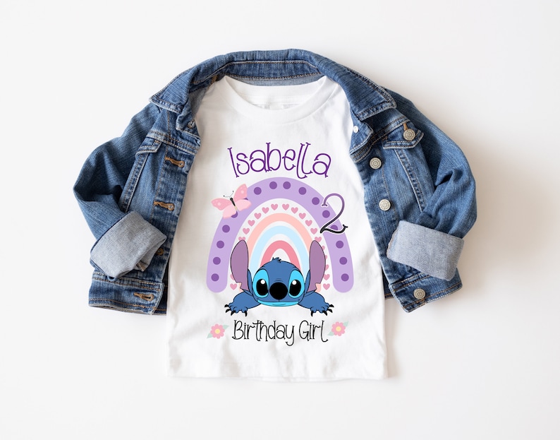 May include: White t-shirt with a purple, pink, and blue rainbow with a blue Stitch character peeking out from behind it. The text "Isabella 2 Birthday Girl" is printed on the shirt.