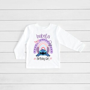 May include: White long-sleeved shirt with a purple rainbow, a blue Stitch character, and the text "Isabella 2 Birthday Girl".