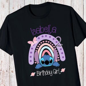 May include: Black t-shirt with a purple, pink, and blue rainbow with a Stitch character peeking out from behind it. The text "Isabella 2 Birthday Girl" is printed on the shirt.