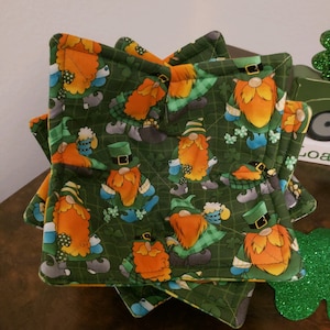 May include: Set of four green, yellow, and orange fabric pot holders with a pattern of gnomes wearing green hats and holding shamrocks.
