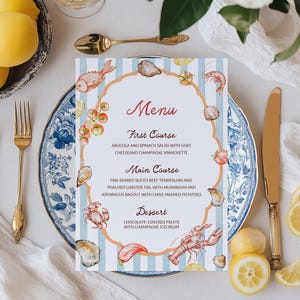 Könnte beinhalten: Eine elegante Tischdekoration mit einer Menükarte mit Meeresfrüchte-Illustrationen. Goldene Besteck, weiße Rosen und blau-weißes Porzellan umgeben die Speisekarte. Auf der Menükarte steht das Wort "Menu" in Rot.