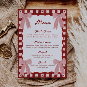 May include: A menu card with a burgundy border and a white interior, featuring a menu for a multi-course meal. The menu includes courses like Smoked Salmon Roulade and Gingerbread Cheesecake. Pink bows decorate the corners.