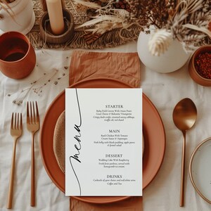 Może przedstawiać: Biała karta menu z ręcznie napisanym „menu” w kolorze czarnym po lewej stronie. Menu zawiera przystawkę, danie główne, deser i napoje. Przystawka to sałatka z młodych liści z azjatyckimi gruszkami, serem kozim i winegretem balsamicznym. Danie główne to kurczak z bazylią w sosie śmietanowym z pomidorami i szparagami. Deser to tort weselny z malinami. Napoje to koktajle do wyboru oraz wino czerwone/białe, kawa i herbata.