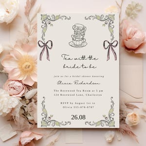 Könnte beinhalten: Eine Einladung zur Brautparty mit cremefarbenem Hintergrund, verziert mit floralen und dekorativen Elementen. Die Einladung enthält den Text "Tea with the bride to be" und Veranstaltungsdetails. Das Design umfasst gestapelte Teetassen und Schleifen.