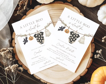 May include: Two baby shower invitations with the text "A Little Boo is almost due." The invitations feature illustrations of a onesie, a ghost, a bat, and a pumpkin. The invitations are on a wooden surface with pumpkins.
