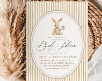 May include: Baby shower invitation with a bunny illustration. The invitation features a beige and white striped background. The text reads "A Little Bunny Is On The Way" and includes event details and RSVP information.