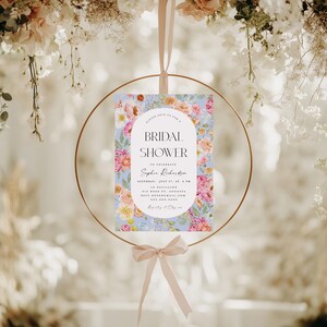 Pu&ograve; includere: Un invito a un bridal shower floreale con uno sfondo blu chiaro e fiori rosa, bianchi e gialli. Il testo recita "Si prega di unirsi a noi per un Bridal Shower per celebrare Sophia Richardson Sabato 17 luglio, alle 18:00 Le Pavillion 515 Rose St, Augusta RSVP: sophiar@email.com Lista nozze: &Egrave; facile"