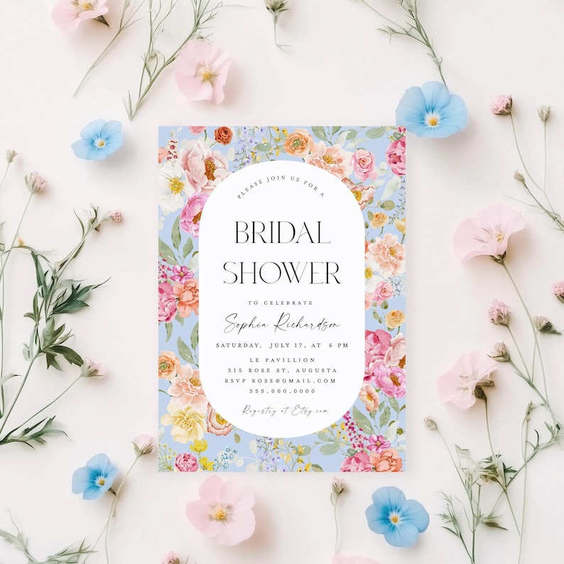 Pu&ograve; includere: Un invito a un bridal shower floreale con sfondo blu chiaro e cornice ovale bianca. Il testo recita "Si prega di unirsi a noi per un bridal shower per celebrare Sophia Richardson, sabato 17 luglio alle 18:00, Le Pavillion, 315 Rose St., Augusta, RSVP rose@gmail.com, 555.000.0000, Registro su Etsy."