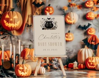 Puede incluir: Un cartel de baby shower con temática de Halloween con un caldero negro, detalles florales y el texto "Bienvenido a la baby shower de Charlotte 26.11.2023".
