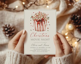 Peut inclure: Une invitation à une soirée cinéma de Noël avec un seau de popcorn rayé rouge et blanc avec un nœud rouge et du popcorn blanc. Le texte indique "Christmas Movie Night" et "Please join us to celebrate Olivia and James Saturday 21 December at 6 PM The Richardson's Home 21 Moonlight Street Philadelphia, PA Rsvp to Olivia 555.000.0000"