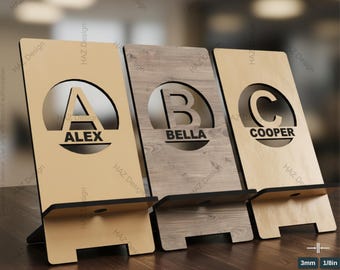 Puede incluir: Tres plantillas de soporte para teléfono de madera con el texto "PHONE STAND TEMPLATES" en la parte superior. Cada soporte tiene un recorte de letra diferente con un nombre debajo: "A ALEX", "B BELLA" y "C COOPER". Los soportes son de madera y tienen una ranura para sostener un teléfono.
