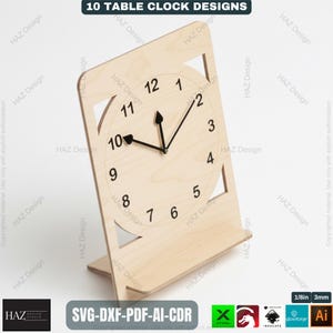 May include: A wooden table clock with a light-colored finish. The clock face features black numerals and hands, with a geometric design around the clock face. The base is rectangular, and the clock is approximately 8 inches tall.