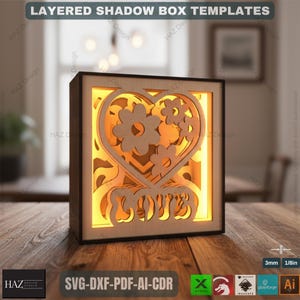 May include: A layered shadow box template with a heart and flower design, illuminated from within. The wooden box features the word "LOVE" and the text "LAYERED SHADOW BOX TEMPLATES". The box is 3mm or 1/8in thick.