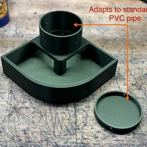 May include: A green 3D printed adapter for a 3-inch PVC pipe. The adapter has a round opening and a rectangular base with a curved edge. The adapter is designed to fit a standard 3-inch PVC pipe.